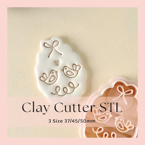 May include: A white clay cutter with a bird design, a bow, and the text "Clay Cutter STL". The cutter has three sizes: 37mm, 45mm, and 50mm. The cutter is on a light pink background.