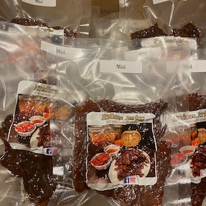 Puede incluir: Seis bolsas de carne seca de vacuno al vac&iacute;o, etiquetadas como "Mild" y "Endless Jerky", con un logotipo rojo y blanco que muestra un frasco de carne seca y el texto "Sabor tradicional de carne seca".