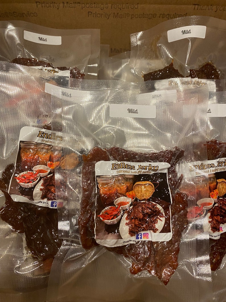 Puede incluir: Seis bolsas de carne seca de vacuno al vac&iacute;o, etiquetadas como "Mild" y "Endless Jerky", con un logotipo rojo y blanco que muestra un frasco de carne seca y el texto "Sabor tradicional de carne seca".