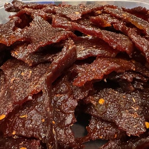 Puede incluir: Primer plano de un bol lleno de cecina de ternera roja oscura. La cecina est&aacute; cortada en tiras finas y tiene una superficie brillante y ligeramente pegajosa.