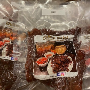 Puede incluir: Primer plano de una bolsa de carne seca de vacuno al vac&iacute;o etiquetada como "Emmer's Jerky" con las palabras "Traditional Beef Jerky" y "Follow us" con iconos de redes sociales. La bolsa est&aacute; etiquetada como "Mild".