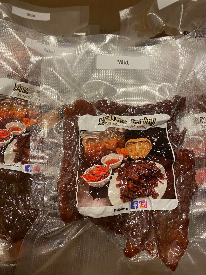 Puede incluir: Primer plano de una bolsa de carne seca de vacuno al vac&iacute;o etiquetada como "Emmer's Jerky" con las palabras "Traditional Beef Jerky" y "Follow us" con iconos de redes sociales. La bolsa est&aacute; etiquetada como "Mild".