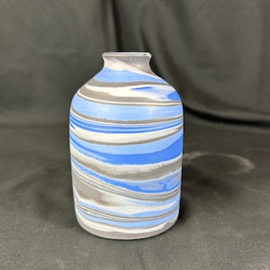 May include: A small, blue and gray ceramic vase with a marbled design. The vase has a rounded body and a narrow neck.
