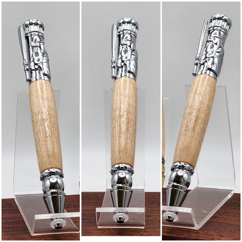 May include: A wooden pen with a silver baseball player design on the top. The pen is on a clear acrylic stand.