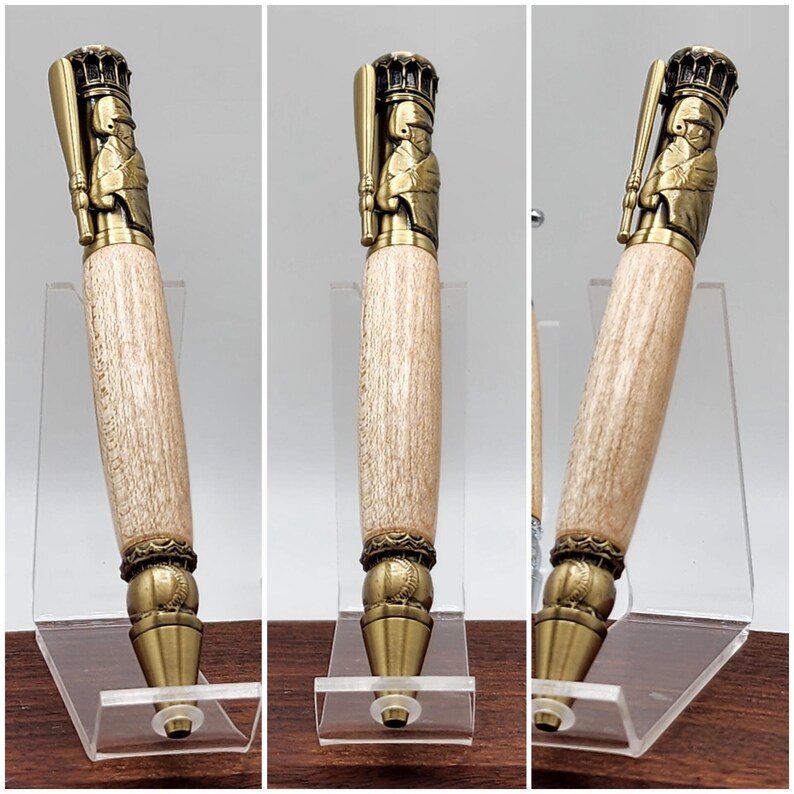 May include: A wooden pen with a gold-toned baseball player topper. The pen is displayed on a clear acrylic stand. The pen has a baseball-themed design at the bottom.