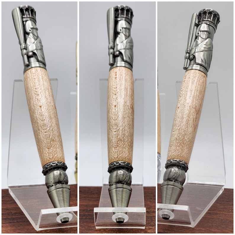 May include: A silver baseball player pen with a wood barrel and a silver baseball cap. The pen is on a clear acrylic stand.