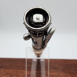 May include: A silver pen with a detailed design resembling a building. The pen has a black clip and a silver cap with a small, square button on top.