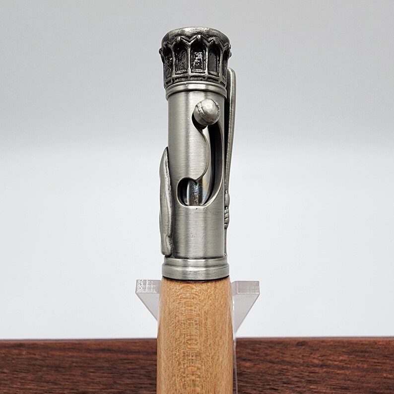 May include: A silver pen with a detailed design on the top and a wooden barrel. The pen is on a clear acrylic stand.