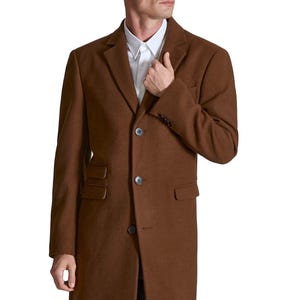 May include: A brown overcoat with a classic design. The coat features a notched lapel, three-button closure, and front pockets. The long coat is made of a wool-like material and is worn over a white dress shirt.