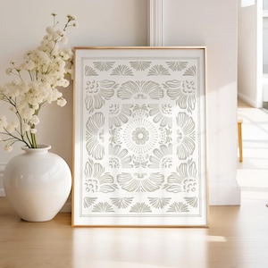 May include: A framed print with a white background and a gray geometric pattern. The pattern is symmetrical and features a central flower design.