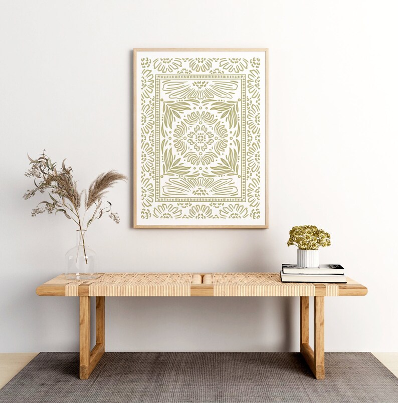 May include: A framed print with a green geometric pattern on a white background. The print is hanging on a white wall above a wooden bench with a woven seat.