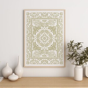 May include: A framed print with a green and white geometric pattern of stylized flowers and leaves. The print is in a light wood frame and is hanging on a white wall.