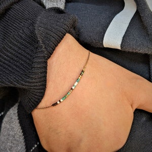 Könnte beinhalten: Ein zartes Armband mit einer dünnen goldenen Kette und kleinen bunten Perlen. Die Perlen sind in den Farben Türkis, Weiß, Braun und Gold.