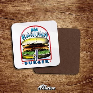 May include: White square coaster with a cartoon burger design. The coaster features the text "BIG KAHUNA BURGER" in blue and red, with a surfer and surfboard graphic. A second brown coaster is next to it.