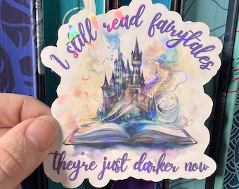 May include: A sticker with a watercolor background featuring a castle and an open book. The sticker has iridescent glitter and the text "I still read fairytales they're just darker now".