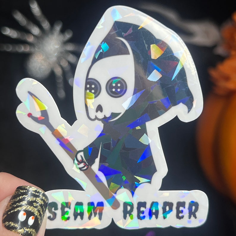 May include: A holographic sticker featuring a cartoon Grim Reaper holding a needle and thread. The sticker says "SEAM REAPER" in a holographic font.