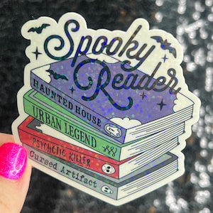 Op de afbeelding: Een holografische sticker met de tekst "Spooky Reader" en een stapel boeken met de titels "Haunted House", "Urban Legend", "Psychotic Killer" en "Cursed Artifact".