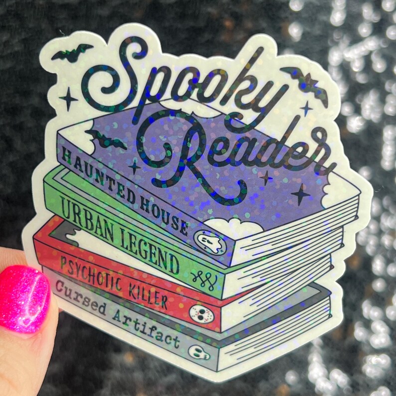 Op de afbeelding: Een holografische sticker met de tekst "Spooky Reader" en een stapel boeken met de titels "Haunted House", "Urban Legend", "Psychotic Killer" en "Cursed Artifact".