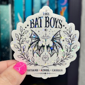 Pu&ograve; includere: Un adesivo olografico bianco con un design nero di due ali di pipistrello con una luna crescente e stelle. Il testo "The Bat Boys" &egrave; in cima all'adesivo. Il testo "Rhysand + Azriel + Cassian" &egrave; in fondo all'adesivo.