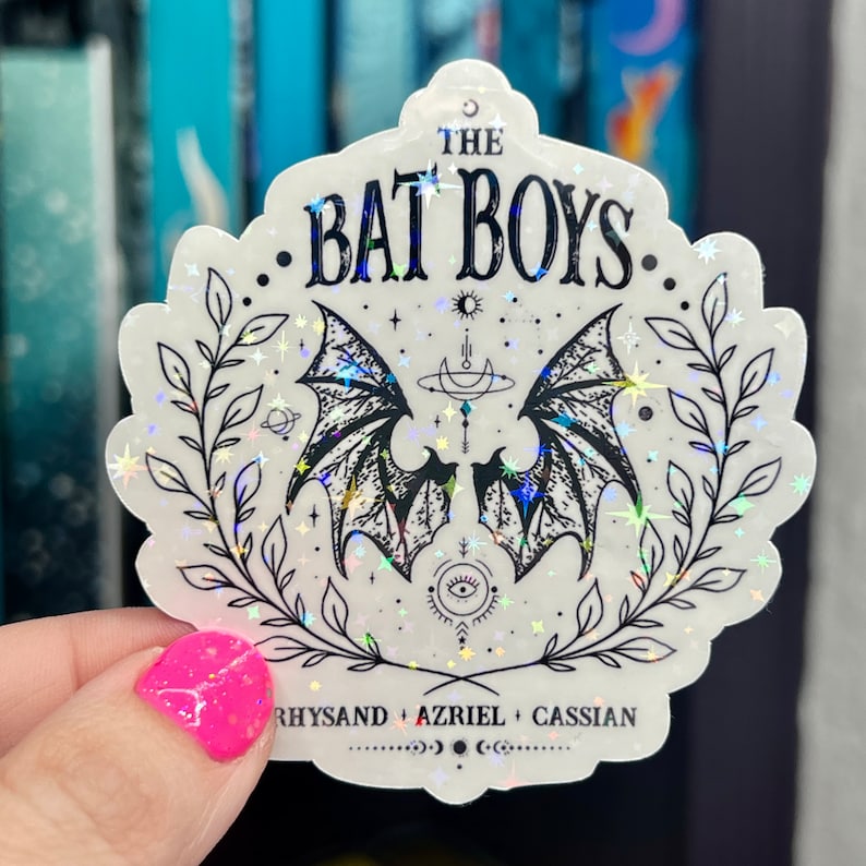 Pu&ograve; includere: Un adesivo olografico bianco con un design nero di due ali di pipistrello con una luna crescente e stelle. Il testo "The Bat Boys" &egrave; in cima all'adesivo. Il testo "Rhysand + Azriel + Cassian" &egrave; in fondo all'adesivo.