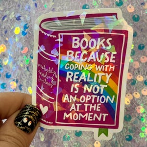 May include: A sticker featuring a stylized book design in shades of pink and purple. The sticker has the text "BOOKS BECAUSE COPING WITH REALITY IS NOT AN OPTION AT THE MOMENT" with a rainbow graphic.
