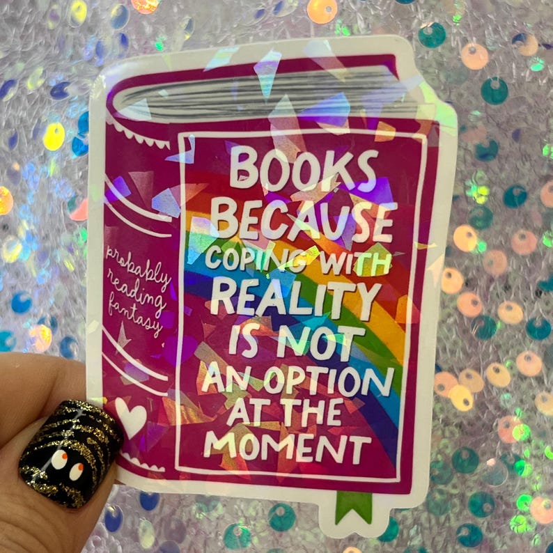 May include: A rectangular sticker with a pink background and the words "BOOKS BECAUSE COPING WITH REALITY IS NOT AN OPTION AT THE MOMENT." The sticker has a rainbow design and the words "probably reading fantasy."