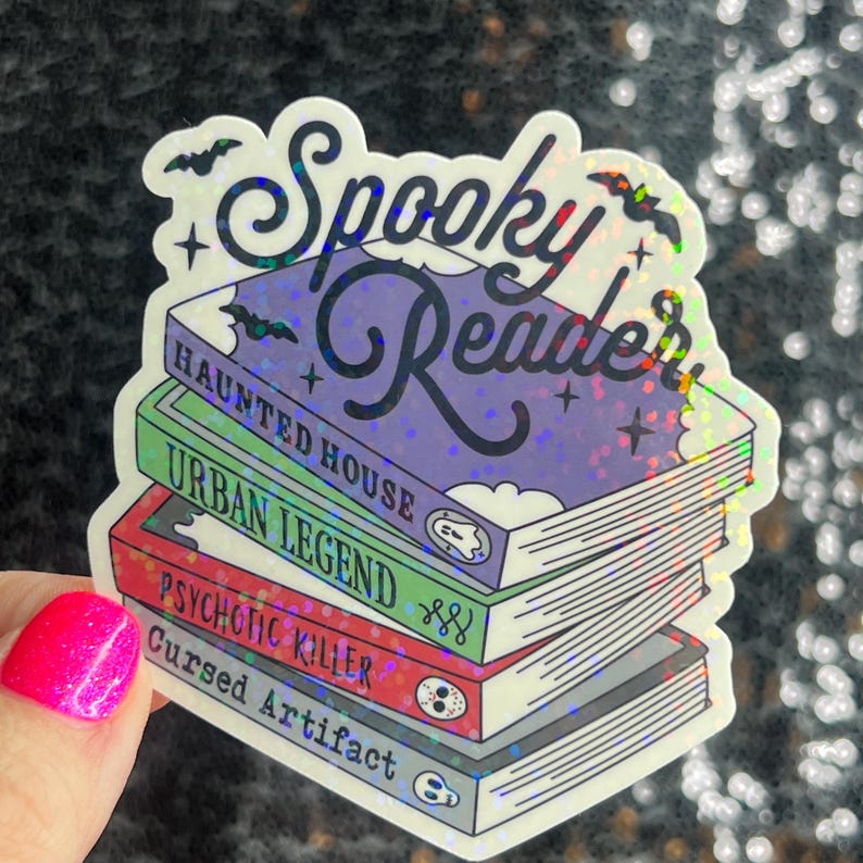 Op de afbeelding: Een holografische sticker met de tekst "Spooky Reader" en een stapel boeken met de titels "Haunted House", "Urban Legend", "Psychotic Killer" en "Cursed Artifact".