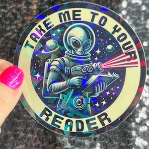 May include: Holographic sticker featuring an alien in a spacesuit holding a ray gun and a book. The text on the sticker reads "TAKE ME TO YOUR READER" in a circular design. The alien is set against a starry background with planets.