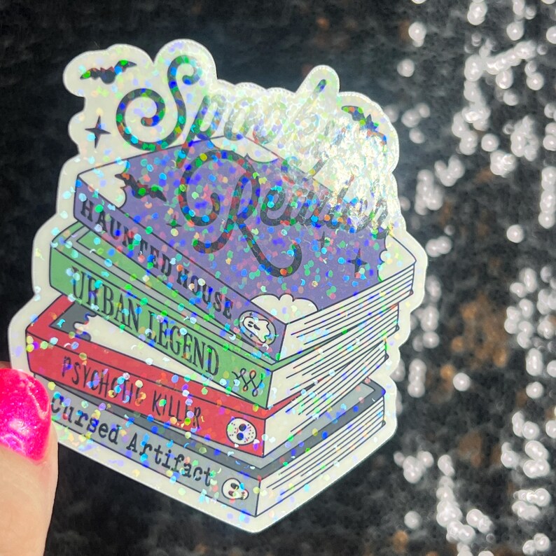 Op de afbeelding: Een holografische sticker met de tekst "Spooky Reads" en een stapel boeken met de titels "Haunted House", "Urban Legend", "Psychic Killer" en "Cursed Artifact".