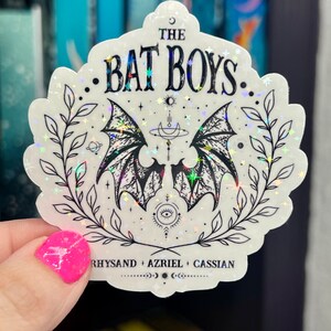 Pu&ograve; includere: Un adesivo olografico bianco con un design nero di un paio di ali di pipistrello con una luna crescente e stelle. Il testo "THE BAT BOYS" &egrave; in cima all'adesivo. Il testo "RHYSAND + AZRIEL + CASSIAN" &egrave; in fondo all'adesivo.