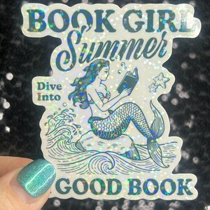 Może przedstawiać: Holograficzna naklejka z napisem "BOOK GIRL Summer" i "Dive Into GOOD BOOK". Naklejka przedstawia syrenę czytającą książkę siedzącą na skale, z falami i gwiazdami.