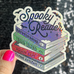 Op de afbeelding: Een holografische sticker met de tekst "Spooky Reader" bovenop een stapel van vier boeken met de titels "Haunted House", "Urban Legend", "Psychotic Killer" en "Cursed Artifact".