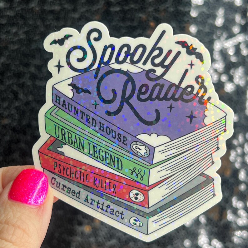 Op de afbeelding: Een holografische sticker met de tekst "Spooky Reader" bovenop een stapel van vier boeken met de titels "Haunted House", "Urban Legend", "Psychotic Killer" en "Cursed Artifact".