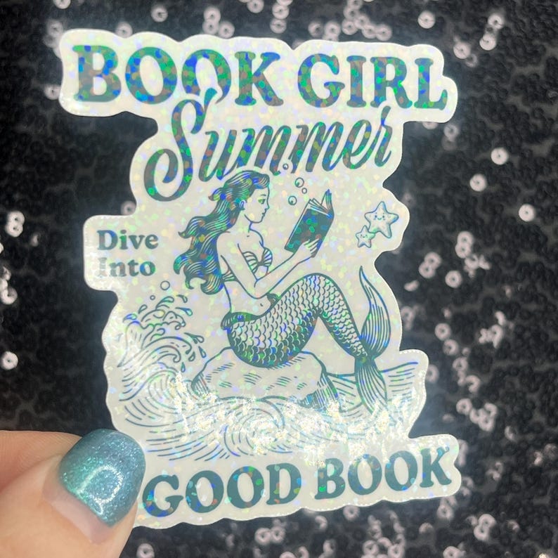 Może przedstawiać: Holograficzna naklejka z syreną czytającą książkę, z napisami "BOOK GIRL SUMMER" i "Dive Into GOOD BOOK". Syrena ma turkusowe włosy i łuskowaty ogon. Bąbelki i gwiazda akcentują projekt.