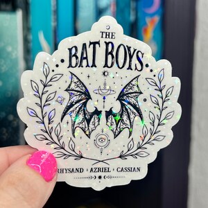 Pu&ograve; includere: Un adesivo bianco con un'illustrazione in bianco e nero di ali di pipistrello, stelle e una luna crescente. Il testo "THE BAT BOYS" &egrave; in cima all'adesivo. Il testo "RHYSAND + AZRIEL + CASSIAN" &egrave; in fondo all'adesivo.
