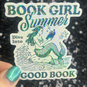 Może przedstawiać: Holograficzna naklejka z syreną czytającą książkę, z napisami "BOOK GIRL SUMMER" i "Dive Into GOOD BOOK". Syrena ma zielone włosy i łuskowaty ogon. W pobliżu unoszą się dwie bąbelki w kształcie gwiazd.