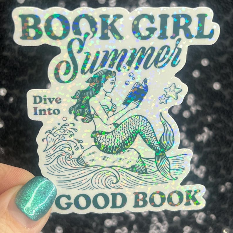 Może przedstawiać: Holograficzna naklejka z syreną czytającą książkę, z napisami "BOOK GIRL SUMMER" i "Dive Into GOOD BOOK". Syrena ma zielone włosy i łuskowaty ogon. W pobliżu unoszą się dwie bąbelki w kształcie gwiazd.