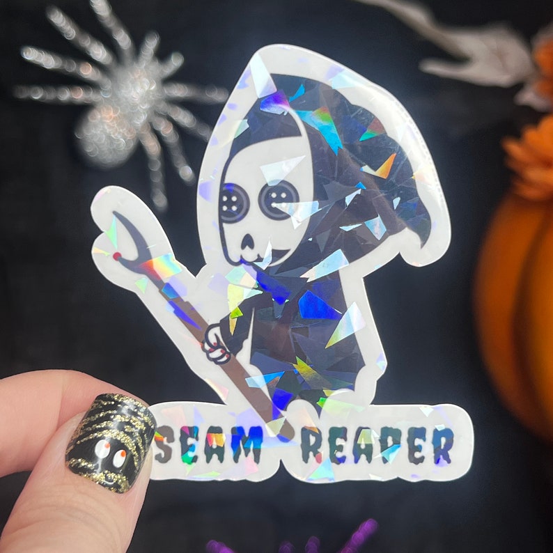 May include: A holographic sticker featuring a cartoon Grim Reaper holding a needle and thread. The sticker says "Seam Reaper" in a holographic font.