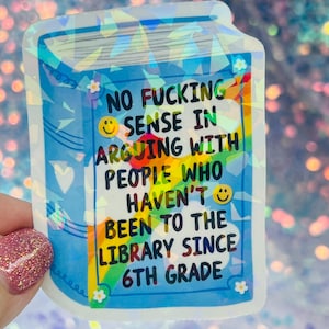 May include: A holographic sticker in the shape of a book with the text "NO FUCKING SENSE IN ARGUING WITH PEOPLE WHO HAVEN'T BEEN TO THE LIBRARY SINCE 6TH GRADE". The sticker has a blue background with white accents and a rainbow gradient.