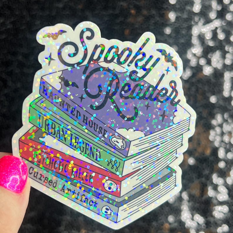 Op de afbeelding: Een holografische sticker met de tekst "Spooky Reader" en een stapel boeken met de titels "Haunted House", "Urban Legend", "Psychotic Killer" en "Cursed Artifact".