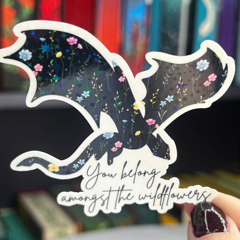 Op de afbeelding: Een zwarte draken-silhouet sticker met een bloemenpatroon en de tekst "You belong amongst the wildflowers".