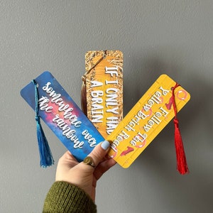 Peut inclure: Trois marque-pages avec des motifs colorés et des glands. Les marque-pages présentent le texte "Si seulement j'avais un cerveau", "Suivez la route de briques jaunes" et "Quelque part au-dessus de l'arc-en-ciel".