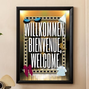 May include: A framed art print with the words "Willkommen, Bienvenue, Welcome" in white against a black background, surrounded by a border of lights. Decorative elements include butterflies and bows. The print hangs on a beige wall.