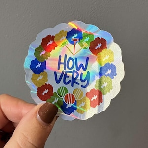 May include: A holographic sticker with a circle of colorful flowers around the text "HOW VERY" in blue and white lettering.