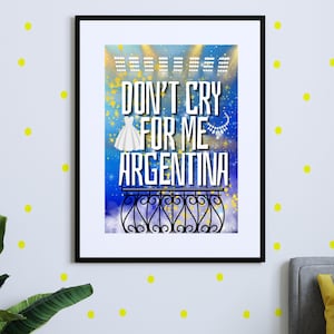 May include: Framed art print with the text "Don't Cry For Me Argentina" in white, featuring a dress and necklace illustration. The background is a blue and yellow gradient with a balcony design at the bottom. The frame is black.