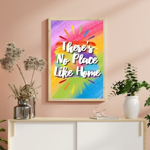 Op de afbeelding: Een ingelijst drukwerk met een kleurrijke abstracte achtergrond en de tekst "There's No Place Like Home" in witte letters.