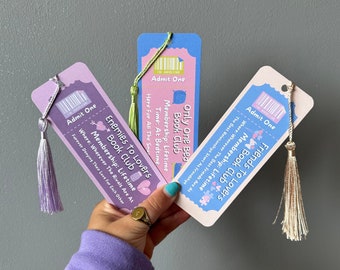 May include: Three colourful bookmarks with a ticket design. Each bookmark has a different book club theme: "Friends to Lovers Book Club", "Enemies to Lovers Book Club", and "Only One Bed Book Club". Each bookmark has a tassel.