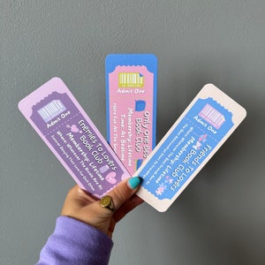 May include: Three colourful ticket-style bookmarks with the text "Friends to Lovers Book Club", "Enemies to Lovers Book Club", and "Only One Bed Book Club". Each bookmark has a different colour scheme and features a cute illustration.