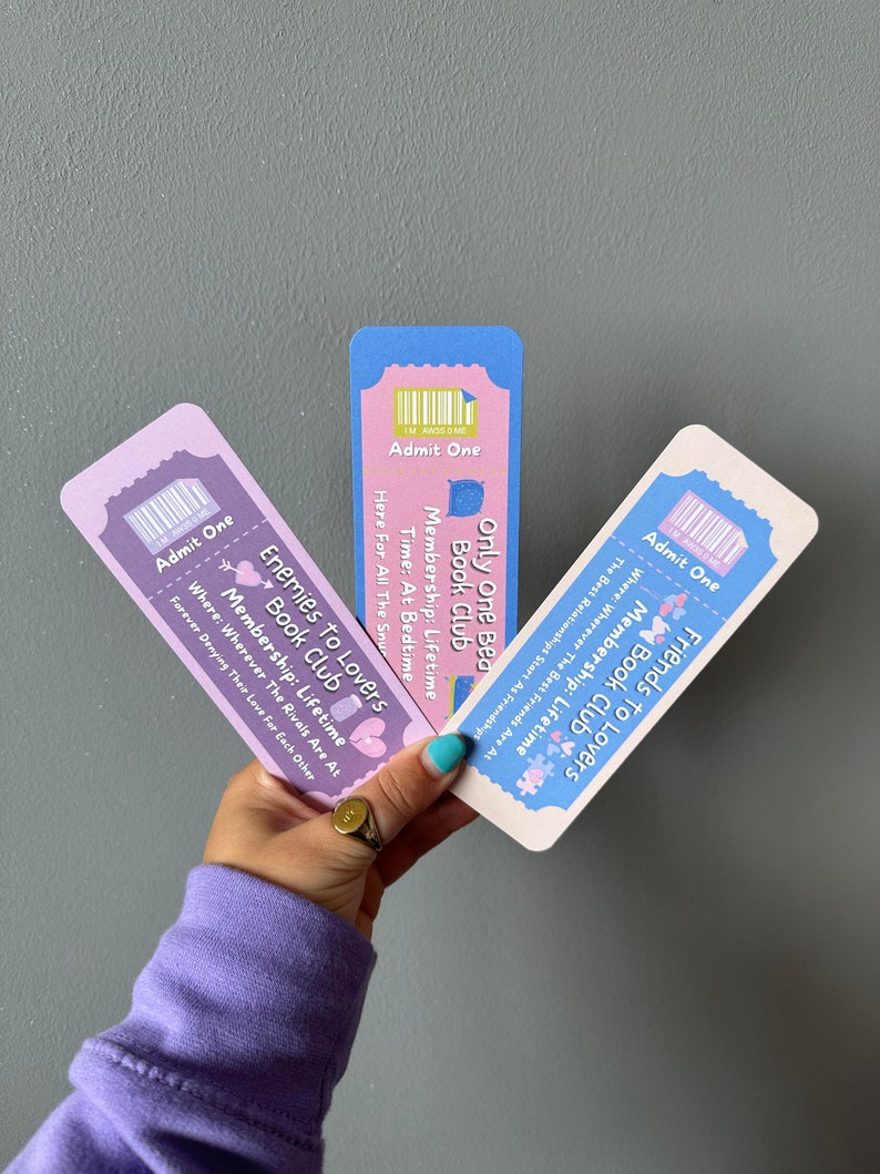 May include: Three colourful ticket-style bookmarks with the text "Friends to Lovers Book Club", "Enemies to Lovers Book Club", and "Only One Bed Book Club". Each bookmark has a different colour scheme and features a cute illustration.