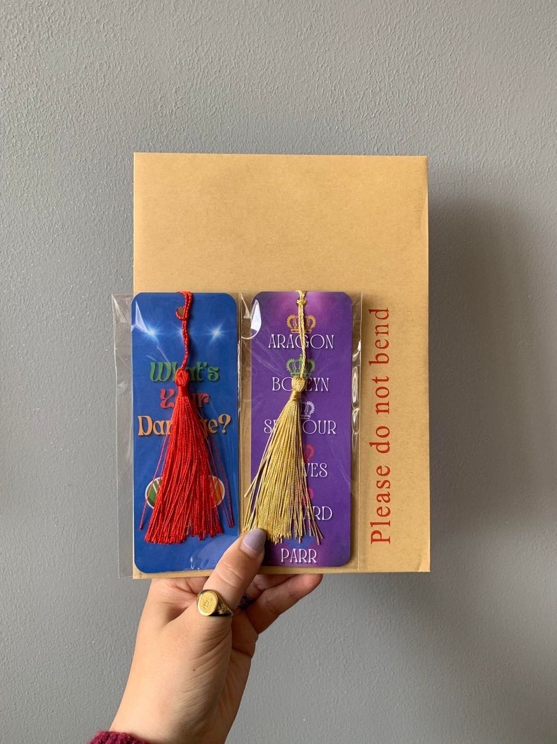 May include: Two purple and blue bookmarks with gold and red tassels. The bookmarks feature text that reads "What's Your Dare?" and "Aragon,  Boelyn, Seymour,  Haves,  Howard, Parr".